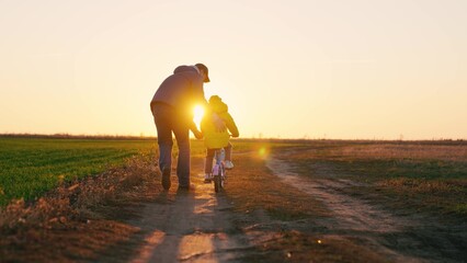 Dad teaches a little girl to ride a children's bike on the road in spring. Happy family. A father...