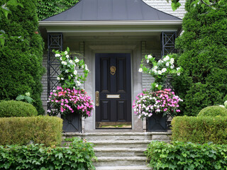 Elegant black and brass front door surrounded by flowers and bushes