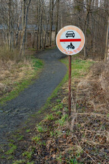 No cars and no motorcycles sign next to a trail leading to a forest on a cloudy day of spring. Traffic sign in remote rural area.