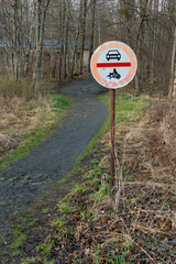 Naklejka premium No cars and no motorcycles sign next to a trail leading to a forest on a cloudy day of spring. Traffic sign in remote rural area.