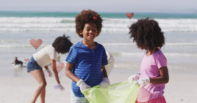 Animation of hearts over african american female and male volunteers picking up rubbish on beach