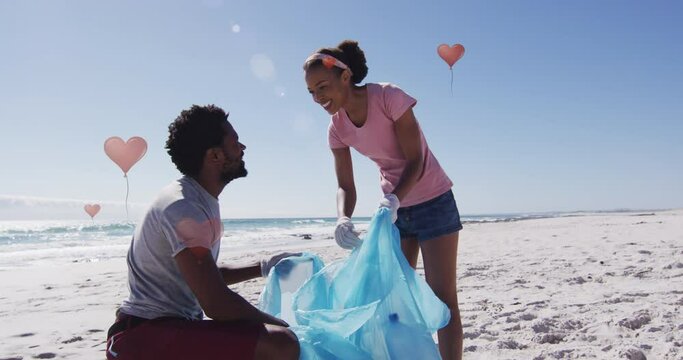 Animation of globe icons over happy african american man and woman picking up rubbish from beach