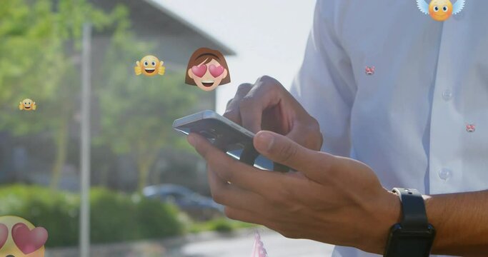 Animation of emoticons over hands of biracial man using smartphone in city
