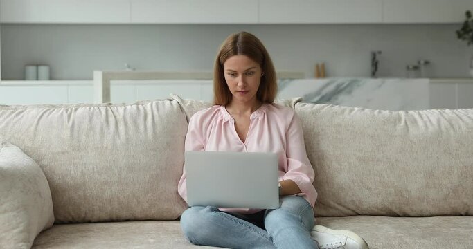 Blogging activity, telecommute, remote job, modern tech usage, freelance concept. Young attractive woman put wireless computer on laps, texting sit on sofa at home, look concentrated, make online task