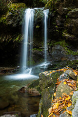 Silky Rainbow Falls waterfall with rocks and fall colored leaves in the foreground in the Great Smoky National Park, Tennessee, USA.