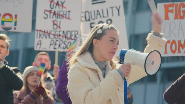 Group of protestors with megaphone holding placards and waving flags on demonstration march to promote gender equality- shot in slow motion