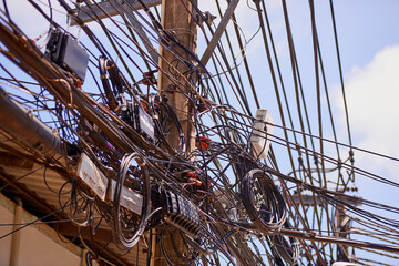 Unplanned urban development. Shot of chaotic telephone and power cables on a post in Thailand.