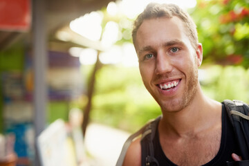 Fototapeta premium Loving backpacking life. Portrait of a smiling young man wearing a backpack traveling in Thailand.