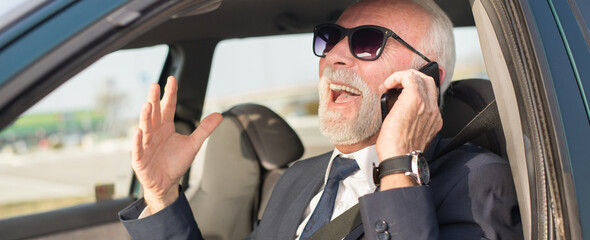 Happy senior businessman talking on the phone while sitting in the car