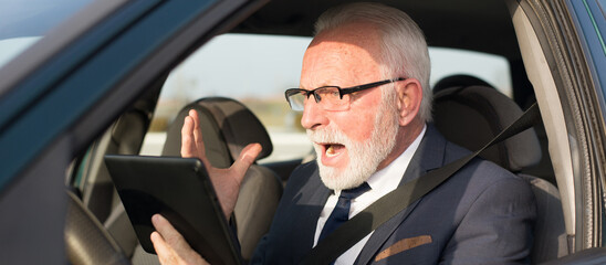 Angry senior businessman using digital tablet in the car	