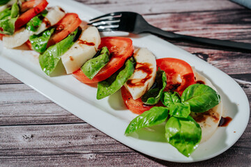 Close up of a Classic Italian caprese salad of mozzarella, tomato and basil with olive oil and vinegar.
