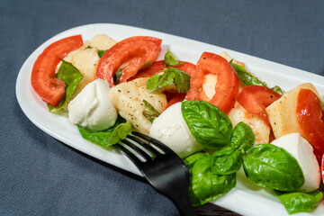Classic Italian caprese salad of mozzarella, tomato and basil with olive oil and vinegar. Close up.