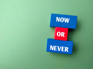 Top view colored wooden block with text NOW OR NEVER on green background.