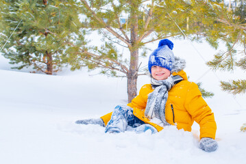 Fototapeta na wymiar cheerful boy playing snowballs in a yellow jacket and a blue hat