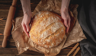The baker's hands holding homemade natural bread with a Golden crust on a napkin on old wooden background. Rustic style.