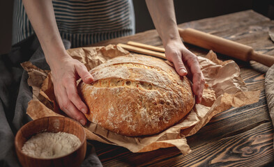 The baker's hands holding homemade natural bread with a Golden crust on a napkin on old wooden background. Rustic style.