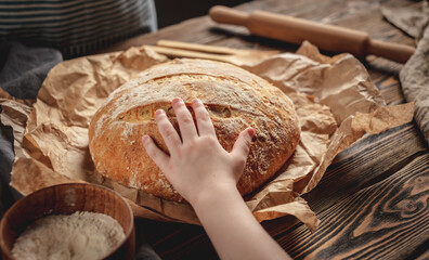A child's hand is touching homemade natural fresh bread with a golden crust on a napkin on an old...