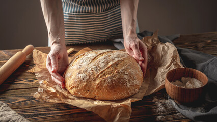 Female hands holding homemade natural bread with a Golden crust on a napkin on an old wooden background. Rustic style