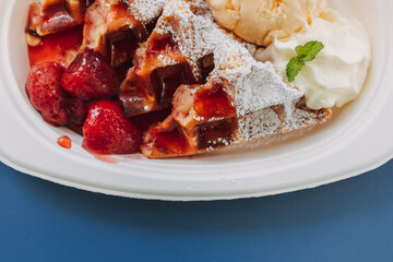 Dessert set of ice-cream waffle with cherries served on blue table.