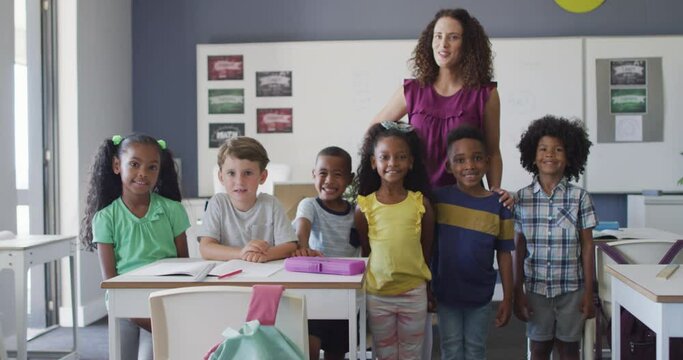 Video of happy caucasian female teacher and class of diverse pupils posing at camera