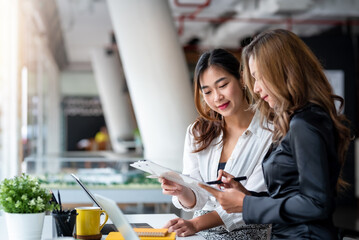 Two young Asian businesswomen talk, consult, discuss working with new startup project idea presentation analyze plan marketing and investment in the office.