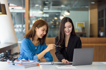Two young Asian businesswomen talk, consult, discuss working with new startup project idea presentation analyze plan marketing and investment in the office.