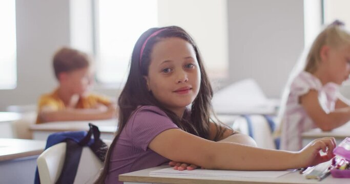 Video of happy caucasian girl sitting at desk in classroom