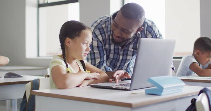 Video of happy african american male teacher helping caucasian girl with laptop
