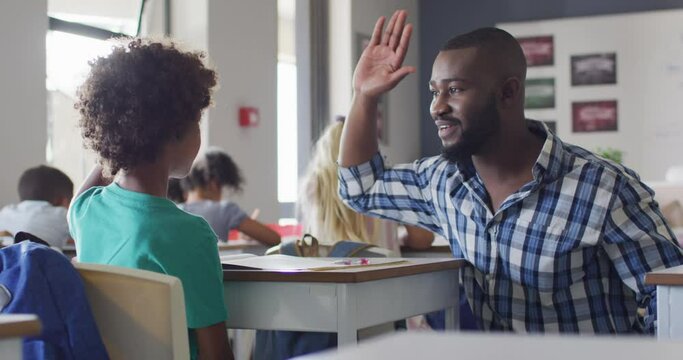 Video of happy african american male teacher clapping hands with african american boy