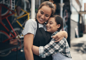 We are actually family. Shot of two young female colleagues sharing a hug outside a bicycle repair...