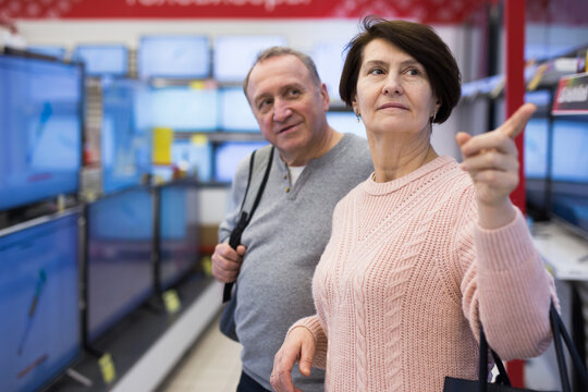 Portrait of a mature European couple in an electronics and home appliance store, standing in the department with televisions