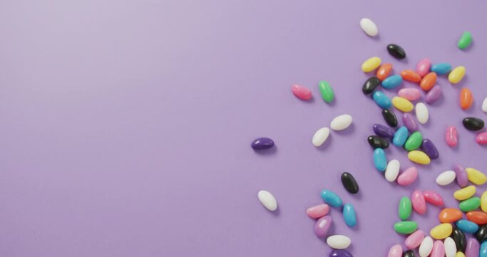 Video of overhead view of multi coloured sweets with copy space over purple background