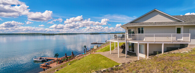 Panoramic view of a beautiful, large modern luxury summer holiday home, featuring sun decks, glass railings, and large windows, set beside a small lake in central British Columbia, Canada. - obrazy, fototapety, plakaty