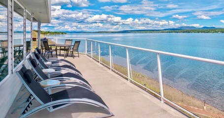 Fototapeta na wymiar Large private home balcony with contemporary glass railings and outdoor deck furniture, overlooking a lake in British Columbia, Canada. 
