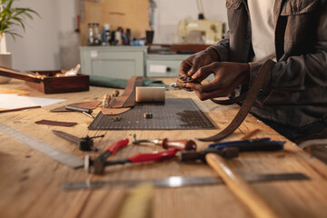 Midsection of african american young craftsman fixing buckle on leather belt in leather workshop