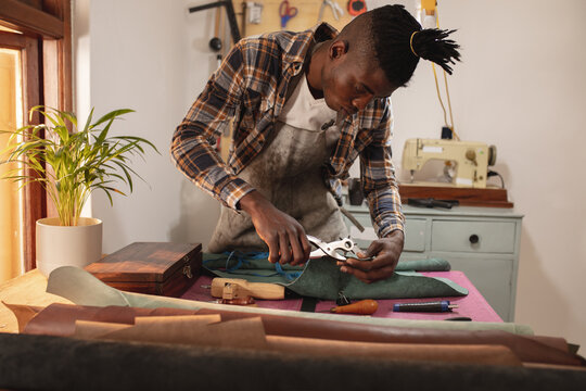 African american young craftsman making holes on leather with punch plier in workshop
