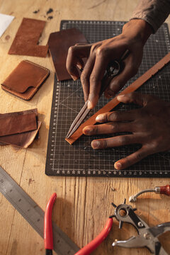 African american young craftsman measuring leather with scratch compass on layer cutting mat