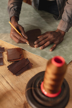 Midsection of african american young craftsman outlining on leather with pencil while making wallet