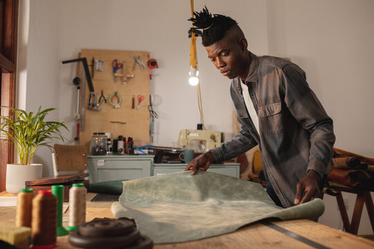 African american young craftsman keeping leather on workbench while working in workshop