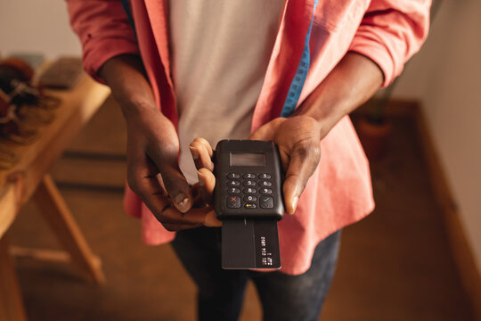 Midsection of african american young male owner holding credit card reader machine in small shop