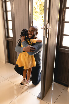 Cheerful african american man kneeling while embracing daughter on arrival at house entrance