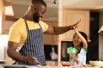 Happy african american daughter and father giving high-five while making pizza in kitchen at home