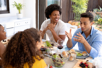 Biracial man talking with friends sitting together for lunch at dining table