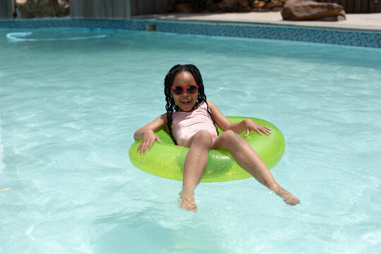 Portrait of smiling cute african american girl wearing sunglasses sitting on inflatable ring in pool
