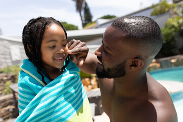 Happy playful african american father touching daughter's nose at poolside on sunny day