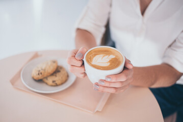 a woman sitting in a cafe holding a specialty coffee with cookies