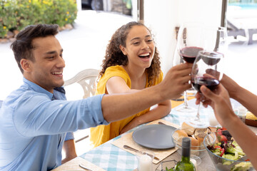 Happy biracial men and women toasting wineglasses while sitting together at dining table