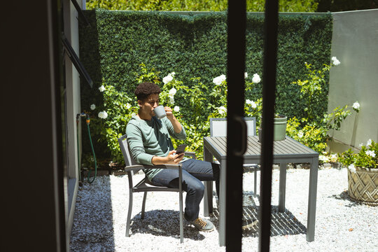 Biracial man drinking coffee while sitting on chair in courtyard on sunny day