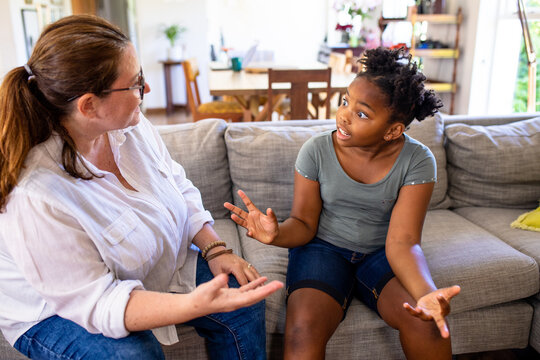 Caucasian mature woman scolding african american daughter gesturing while sitting on sofa at home
