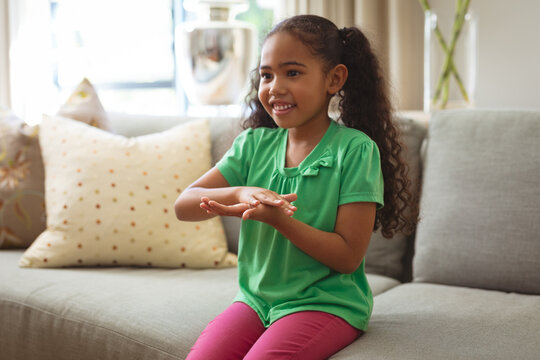 Smiling multiracial mute girl talking through hand sign language sitting on sofa at home